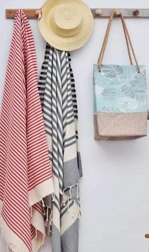 Red and grey striped foutas, a straw hat and a beach bag hanging on a pegboard